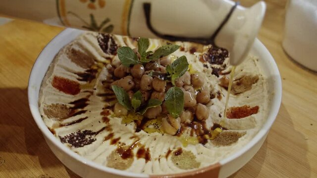 Decorating hummus dish with cumin, paprika, rosemary spices by hand adding paprika, rosemary and fresh mint. Dish decoration. Cooking  Muslim food
