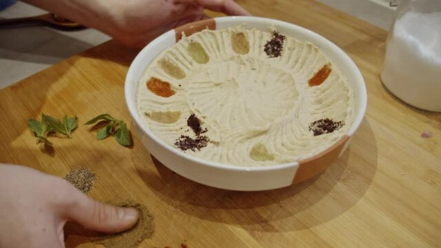 Decorating hummus dish with cumin, paprika, rosemary spices by hand. Dish decoration. Cooking  Muslim food