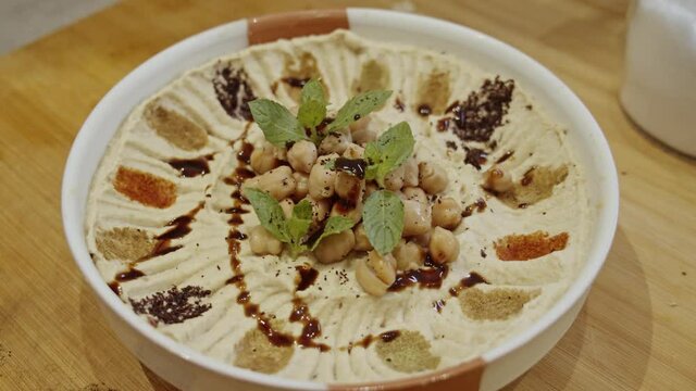 Decorating hummus dish with cumin, paprika, rosemary spices by hand adding paprika, rosemary and fresh mint. Dish decoration. Cooking  Muslim food