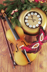 Wall clock, violin and bow, carnival mask, fir branch and Christmas decorations on a wooden background.