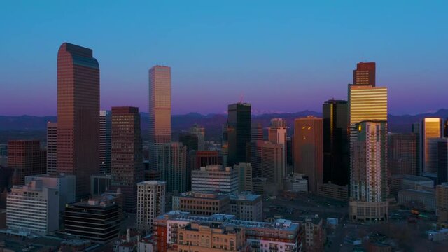 Anamorphic drone footage of Denver skyline with Rocky Mountains in background during blue & golden hour