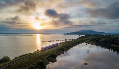Fototapeta na wymiar Aerial view of Sunrise or sunset above Pa Sak Jolasid dam at Lopburi amazing Thailand with silhouette Passenger train run on the railroad tracks among the lake.