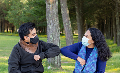 Young man wearing mask greets a young woman wearing mask at a park