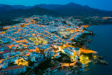 Illuminated evening view from drone of coastal Mediterranean city of Nerja, Andalusia, Spain