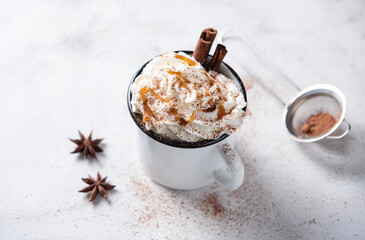 coffee latte with creamy caramel cream and cinnamon in a white mug on a white table.