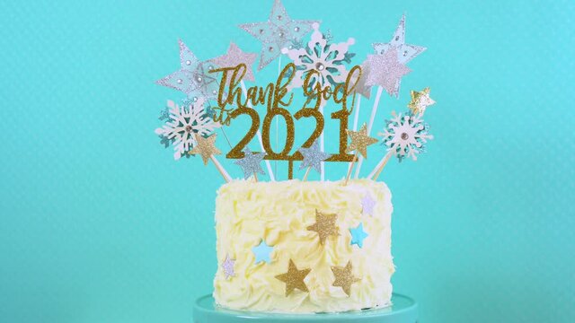 Happy New Year's Eve celebration cake on cake stand in blue white and gold theme decorated with stars and humorous, Thank God It's 2021, cake topper decoration. Closeup rotating.