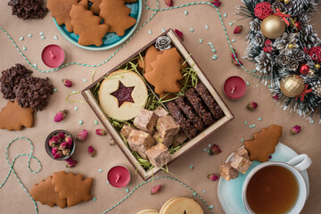 New Year and Christmas flat lay photo of box filled with homemade cakes on craft paper background, with decorations and baking around.