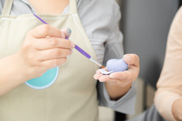 Close up of woman's hands working with fondant to decorate a cake - woman painting clay with paintbrush and coloring