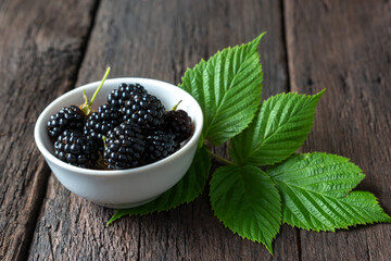 Ripe blackberries in a bowl and foliage on a wooden table. Harvesting season in the home garden