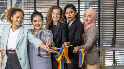 Five business women from different ethnic races and cultures express support for LGBT with flags in an office