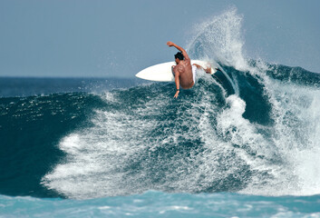A surfer carves a radical off-the-lip on a beautiful blue wave in the ocean. - obrazy, fototapety, plakaty