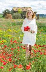 Naklejka na ściany i meble Young woman in white dress walking and holding bouquet of poppies plants outdoor