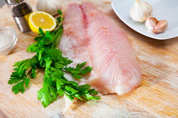 Raw sea perch fillet, garlic, parsley and lemon on wooden table. Ingredients for cooking