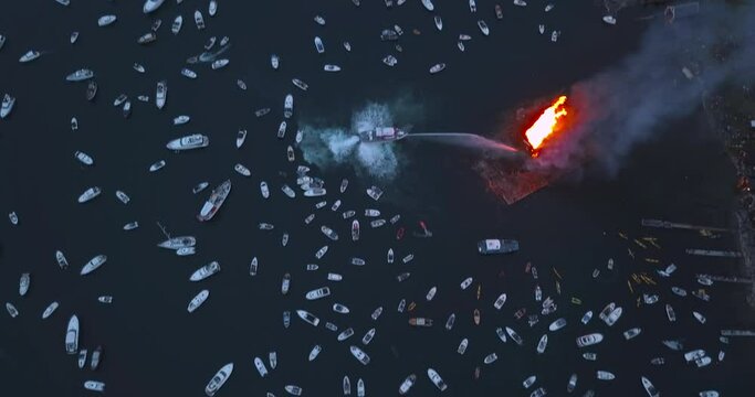 Extremely interesting, high altitude, upward tilting drone footage of small motor boats and sail boats gathering around and witnessing the biggest bonfire event on Earth at Alesund, Norway at dusk.