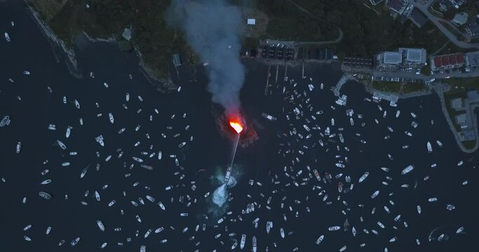 Extremely interesting, high altitude, top down, turning drone footage of small motor boats and sail boats gathering around and witnessing the biggest bonfire event on Earth at Alesund, Norway at dusk.