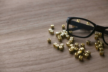 Selective focus of glasses and gold alphabet beads on wooden background with copy space.