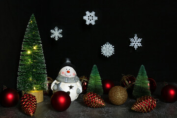snowman with a Christmas tree and Christmas toys on a dark background, snowflakes