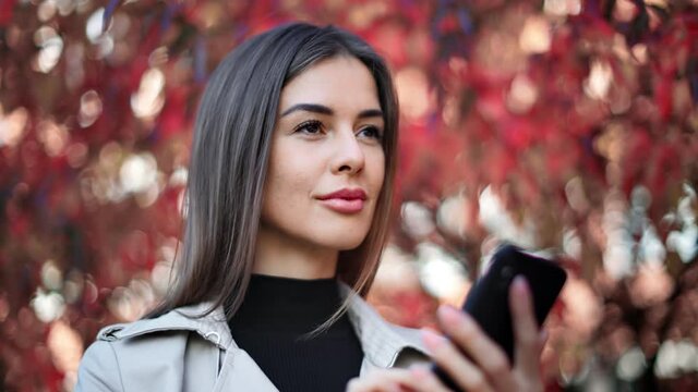 Happy female face chatting use smartphone at red fall foliage bokeh. Close up shot on 4k RED camera