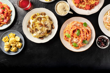 Italian food. Various pastas, olives, wine, grated Parmesan cheese, shot from above, a flat lay on a dark background with a place for text