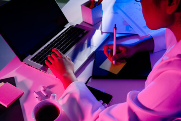 Woman working with laptop at night in neon colored light.