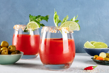Bloody Mary cocktails, garnished with lime and celery, with olives and pickles, a side view on a blue background