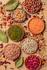 Various legumes, top shot on a brown background. Lentils, soybeans, chickpeas, red kidney beans and other pulses, a flat lay with bay leaves