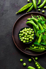Green peas in  bowl with fresh pods on the black concrete background, top view or flat lay