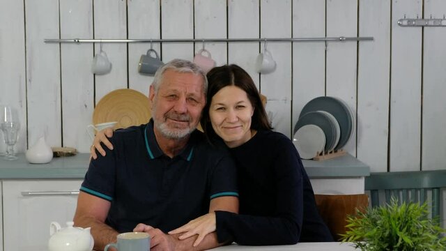 Elderly beared man and adult daughter at the kitchen smiling happily anf hugging, happy family