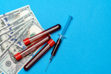 Close up 100 US dollar bills and blood sample in test tube over blue background