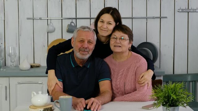 Senior couple and adult daughter at the kitchen smiling happily anf hugging, happy family