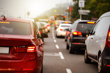 Traffic jam in a city with long queue of cars waiting on a road at sunset. Concept of stress from being late during commute. Street crowded with stopped vehicles.