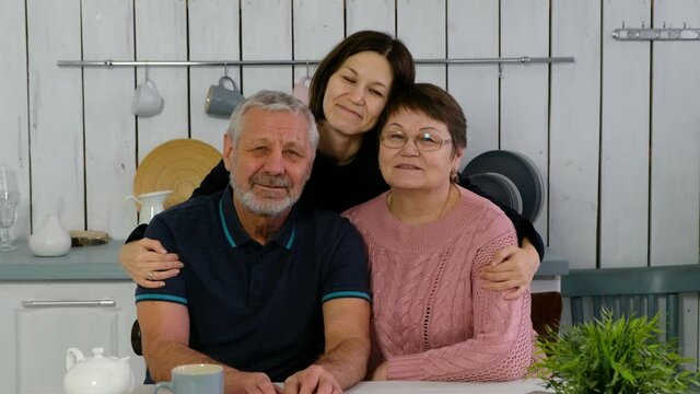 Senior couple and adult daughter at the kitchen smiling happily anf hugging, happy family