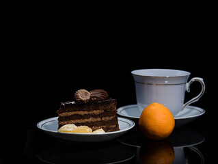 A piece of chocolate cake on a saucer on a black background.