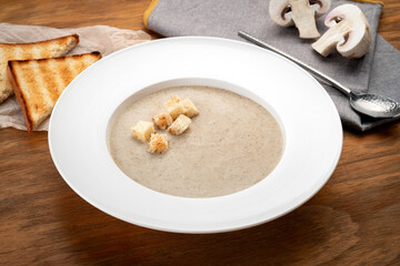 Mushroom soup puree with croutons and mushrooms on a wooden table