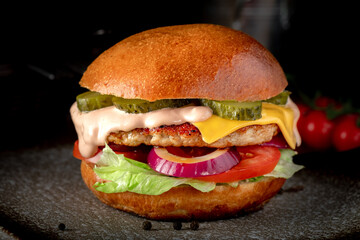 Big BBQ cheeseburger with beef, cheese, tomatoes, cucumbers on a plate on a dark background