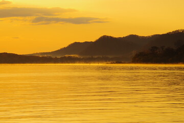 薄いオレンジ色に染まる湖の風景。湖畔の森の影。屈斜路湖、北海道、日本。