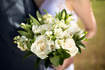 Big nice wedding bouquet in woman's hands. Bride and groom on their wedding hugging.