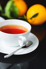 White glass cup with black, red tea with lemon on a dark glass table.