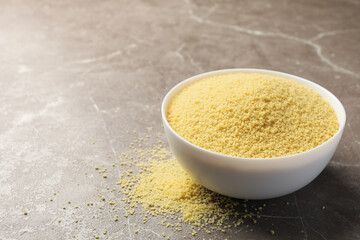 Bowl with raw couscous on gray background