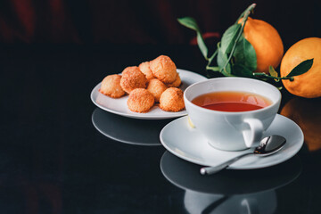 White glass cup with black, red tea with lemon on a dark glass table.