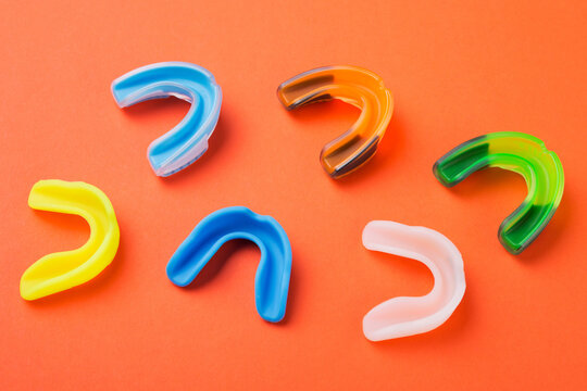 many boxing mouthguards of different colors, lies on an orange background