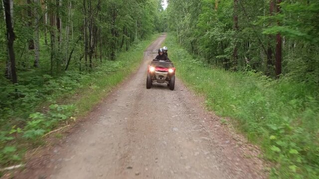 Tracking of people in helmets driving red quad bike along forest road towards camera