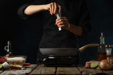 Professional chef pours ground mustard into frying pan for cooking traditional indian curry. Backstage of preparing on dark blue background. Concept of organizing the cooking process. Frozen motion.