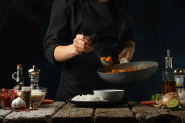 Professional chef pours traditional indian curry on the plate with boiled rice. Backstage of preparing on dark blue background. Concept of serving dinner. Frozen motion.