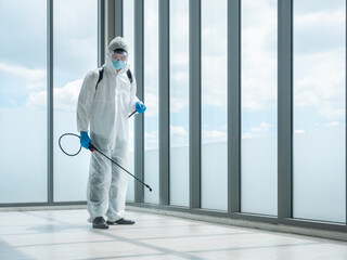 Fototapeta premium Cleaner man hold sterilize spray gun from chemicals sanitizer backpack equipment while wearing face mask, transparent goggles, blue gloves and safety uniform for protect bacteria and virus pandemic