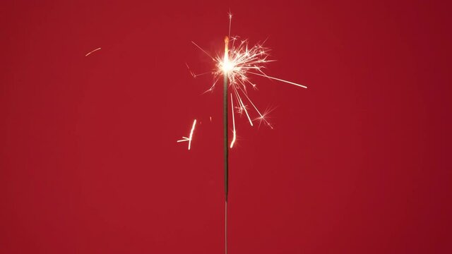 Christmas or Happy New Year concept. Close up banner of Bright burning sparkler on a red background. 4k resolution video