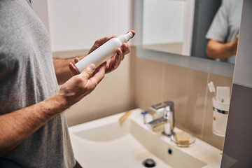Gentleman in grey shirt with white cosmetic bottle in hands
