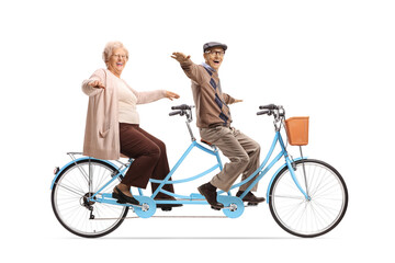 Elderly man and woman riding a blue tandem bicycle and spreading their arms