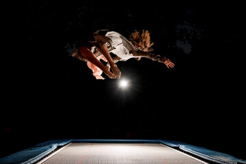handsome woman beautifully jumps on trampoline in the air at dark time