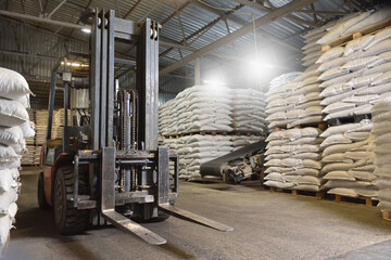 A forklift stands in a warehouse next to pallets with full bags © pridannikov
